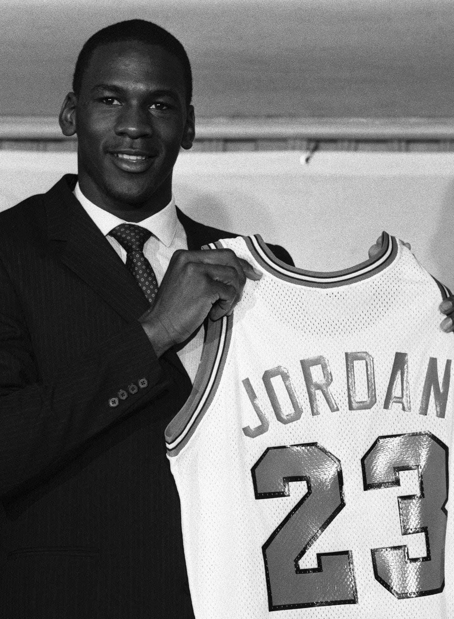 Michael Jordan in a suit holding up a white Chicago Bulls "JORDAN 23" jersey at the September 12, 1984 news conference announcing his signing. Michael Jordan in a suit holding up a white Chicago Bulls "JORDAN 23" jersey at the September 12, 1984 news conference announcing his signing.