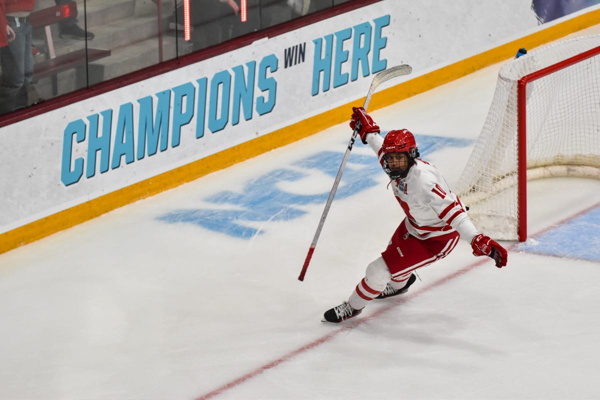 Laila Edwards with both her arms outstretched with hockey rink boards reading 'champions win here' behind her Laila Edwards with both her arms outstretched with hockey rink boards reading 'champions win here' behind her