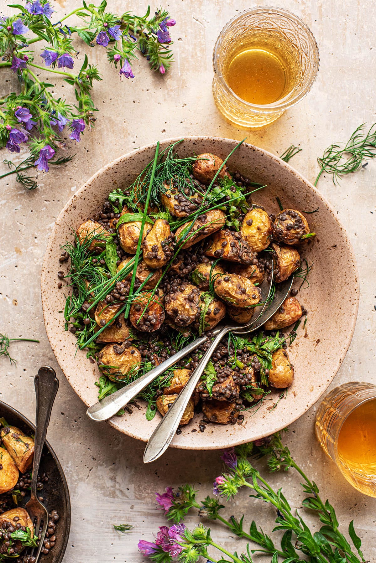 A large bowl of potato salad with lentils and herbs with two serving spoons. A large bowl of potato salad with lentils and herbs with two serving spoons.