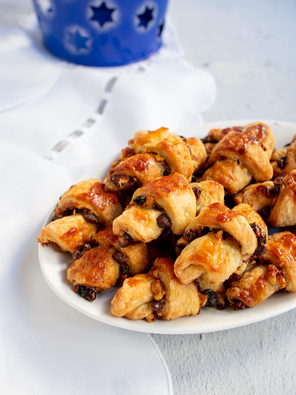 Apricot chocolate rugelach on a white plate with a hanukkah decoration in the background. Apricot chocolate rugelach on a white plate with a hanukkah decoration in the background.