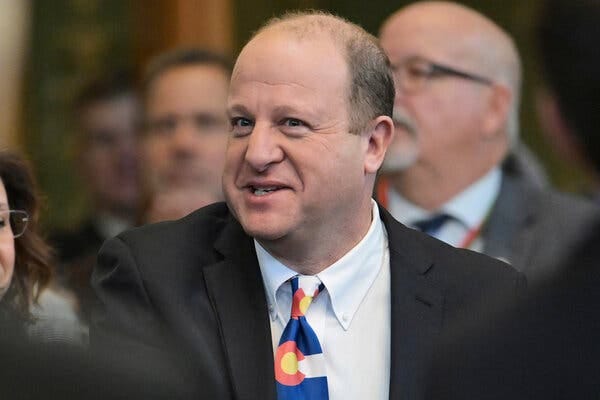 A man in a dark suit and a tie in the pattern of the Colorado flag.