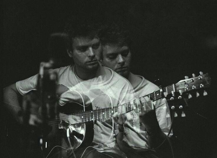 This may contain: two men are playing guitars in the dark