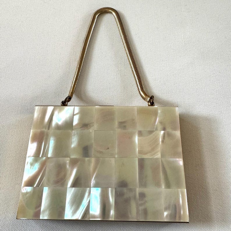 May include: A white rectangular clutch purse with a gold chain strap. The purse is made of mother of pearl tiles.