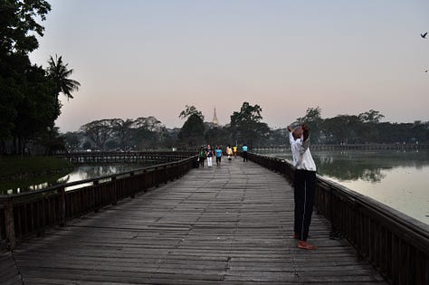 Images of the boardwalk and people exercises in the early morning at Kan Daw Gyi Lake in Yangon. The sun is rising and there is a mist over the water. You can see the golder pagoda Shwe Dagon in the distance.
