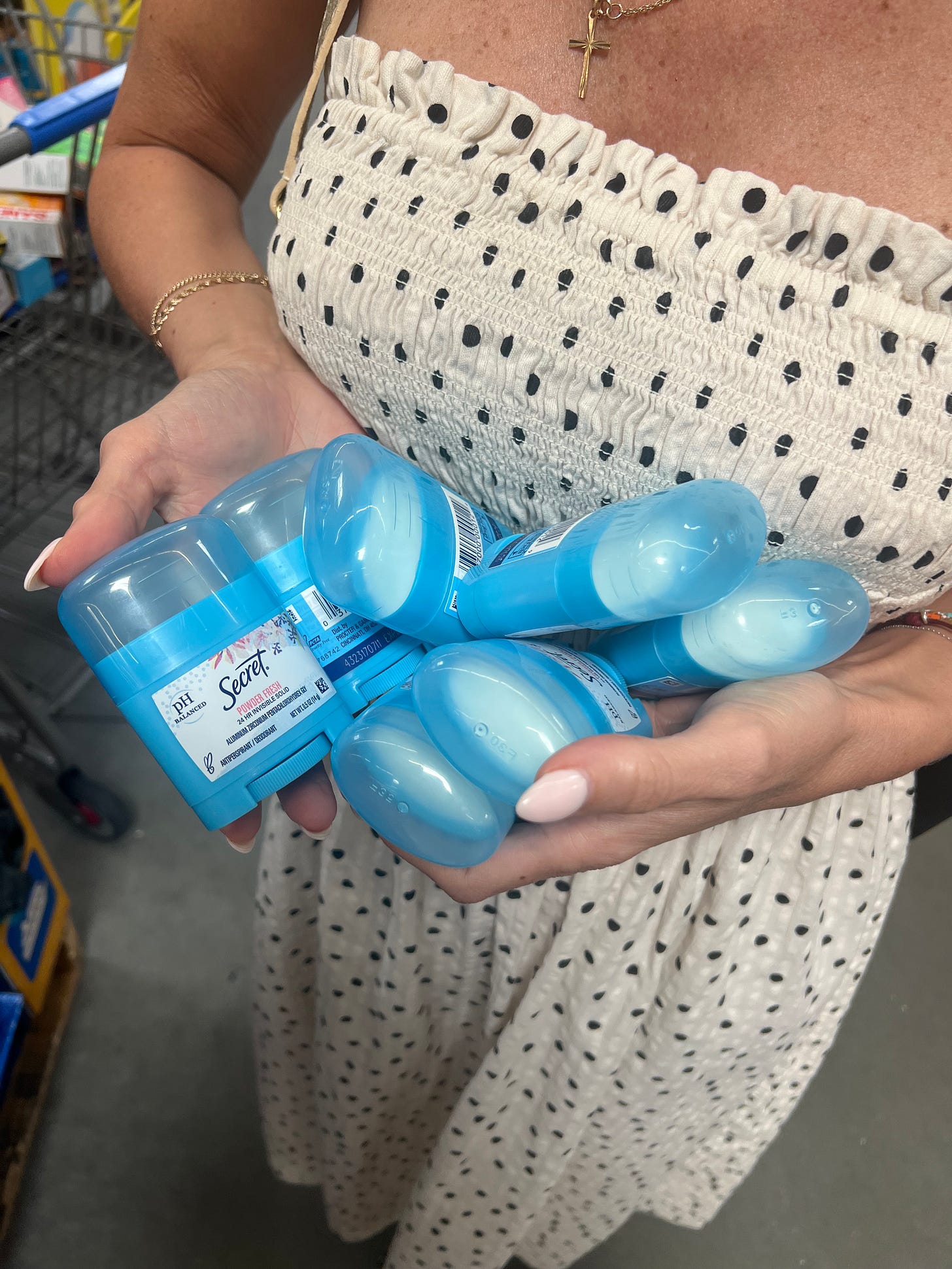 A person wearing a white and black polka-dot strapless dress holding a large handful of blue Secret "Powder Fresh" pH Balanced deodorant sticks while shopping. A person wearing a white and black polka-dot strapless dress holding a large handful of blue Secret "Powder Fresh" pH Balanced deodorant sticks while shopping.