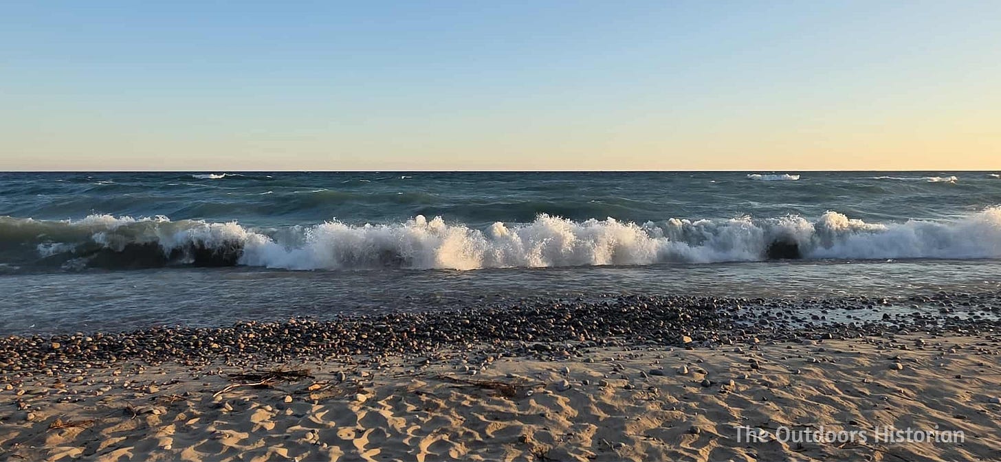 A view of five to six foot tall waves breaking along a sandy beach under the glow of a sunrise.