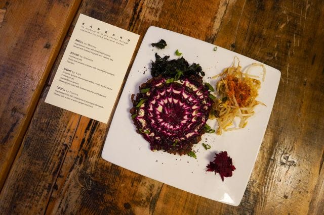 A plate with a pancake covered in a white and magenta cobweb shape, next to a printed menu