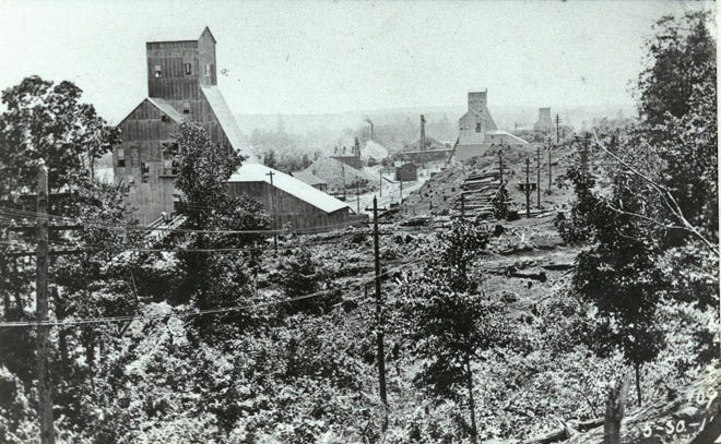 A grainy, black and white historic photograph of the Champion Mine in Painesdale. The image shows the massive shaft house and industrial infrastructure that dominated the landscape in the early twentieth century..