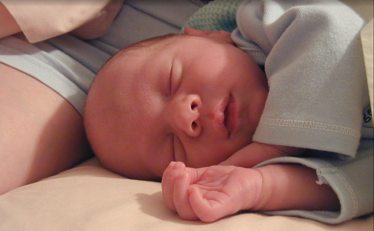 Newborn on their side facing camera, sleeping comfortably.