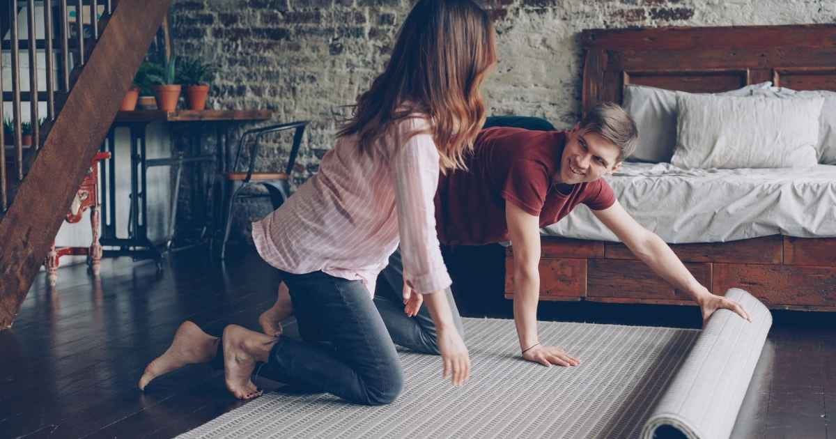 A couple unrolling a carpet in a stylish, industrial-themed bedroom with a brick wall A couple unrolling a carpet in a stylish, industrial-themed bedroom with a brick wall