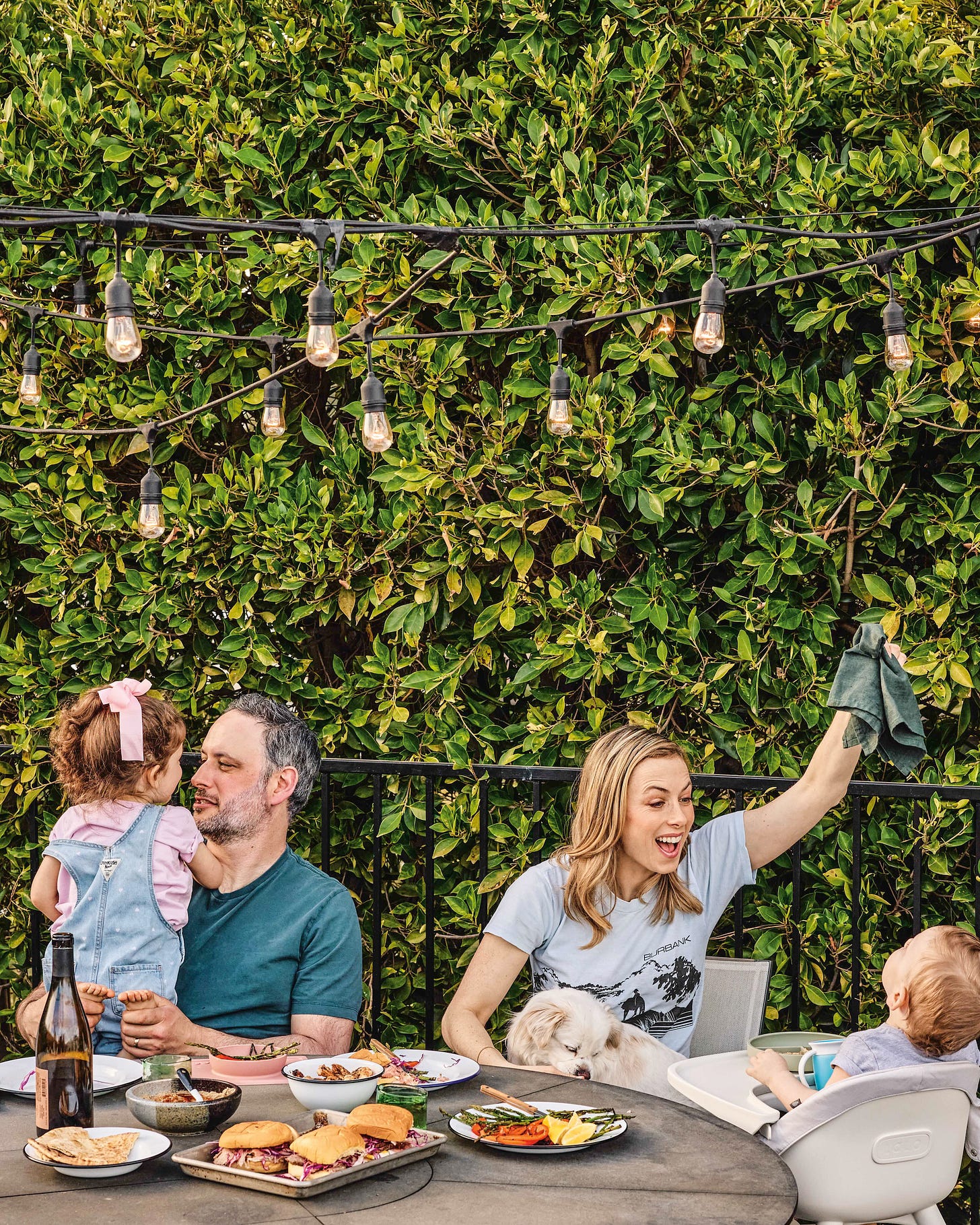 Noah Galuten sitting outside around a round table with plates of food with his wife and two kids