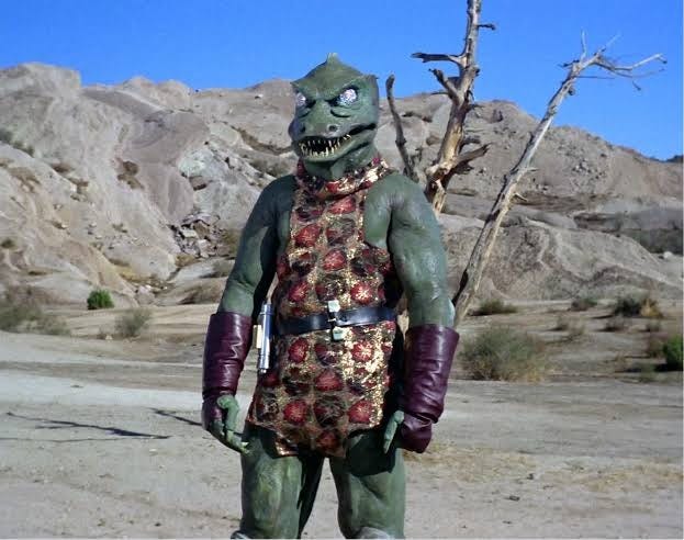 The original Gorn captain from Star Trek stands in a rocky desert landscape, wearing a patterned tunic and purple gloves. The original Gorn captain from Star Trek stands in a rocky desert landscape, wearing a patterned tunic and purple gloves.