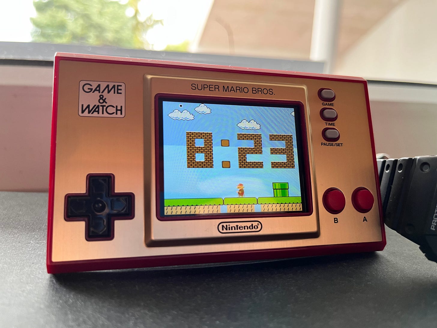 Game & Watch propped up with the clock on the screen showing 8:23.