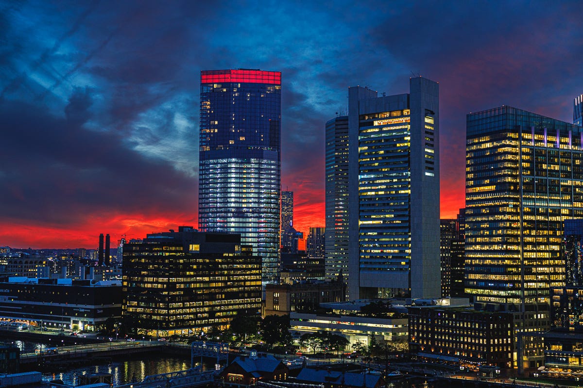 Boston skyline at twilight with darkening red clouds and reflective glass towers.