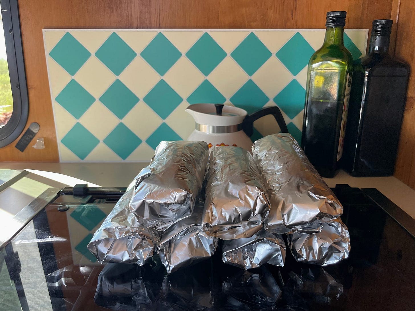 seven burritos wrapped in tinfoil on a glass counter top