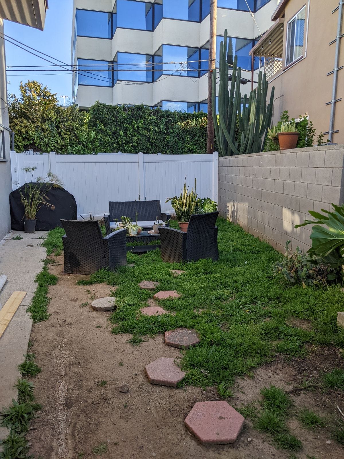 An outdoor garden with green grass and three chairs arranged in a circle.