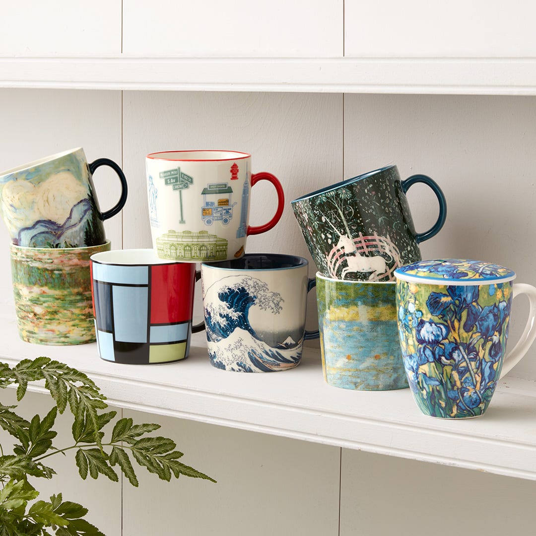 8 mugs featuring various works from The Met collection stand artfully stacked on a white shelf.