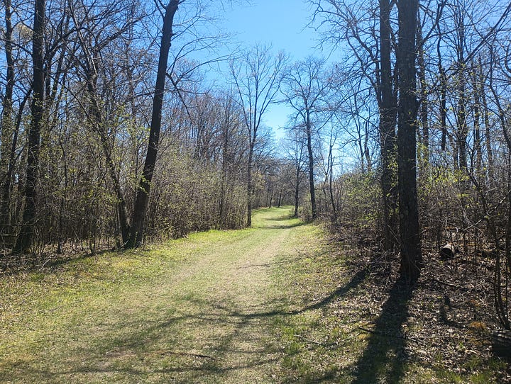 two images of the trail, with green grass and trees; the left photo also has a bench