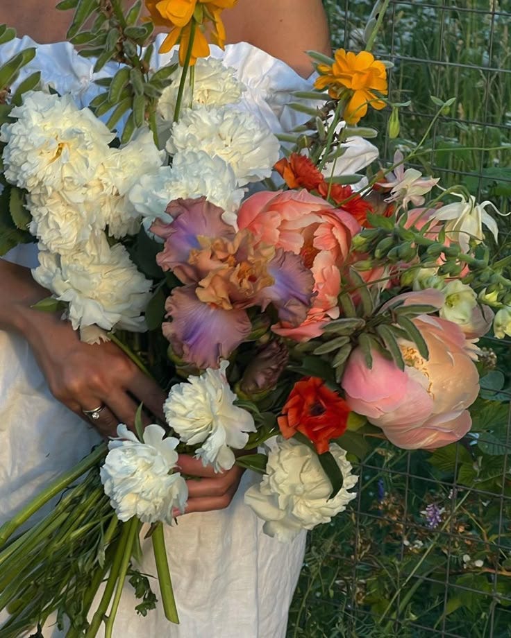This may contain: a woman holding a bouquet of flowers in her hands and wearing a white wedding dress