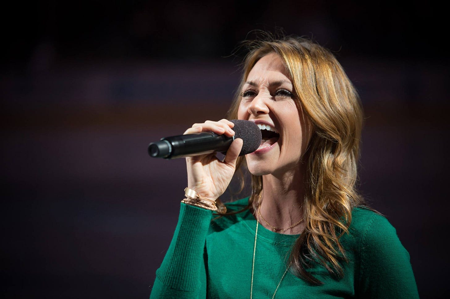 Celena Rae singing into a handheld microphone while wearing a green sweater Celena Rae singing into a handheld microphone while wearing a green sweater