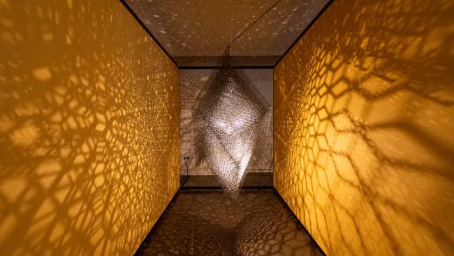 Une sculpture en acier projette, par un jeu d'ombres, des formes géométriques sur les murs dorés attenant