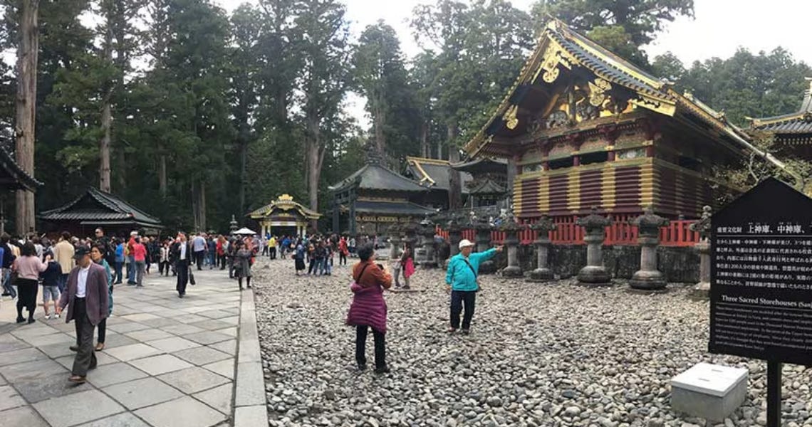 A crowded courtyard at the Nikko Toshogu Shrine in Japan, showing traditional ornate gold and red wooden architecture surrounded by tall cedar trees. A crowded courtyard at the Nikko Toshogu Shrine in Japan, showing traditional ornate gold and red wooden architecture surrounded by tall cedar trees.