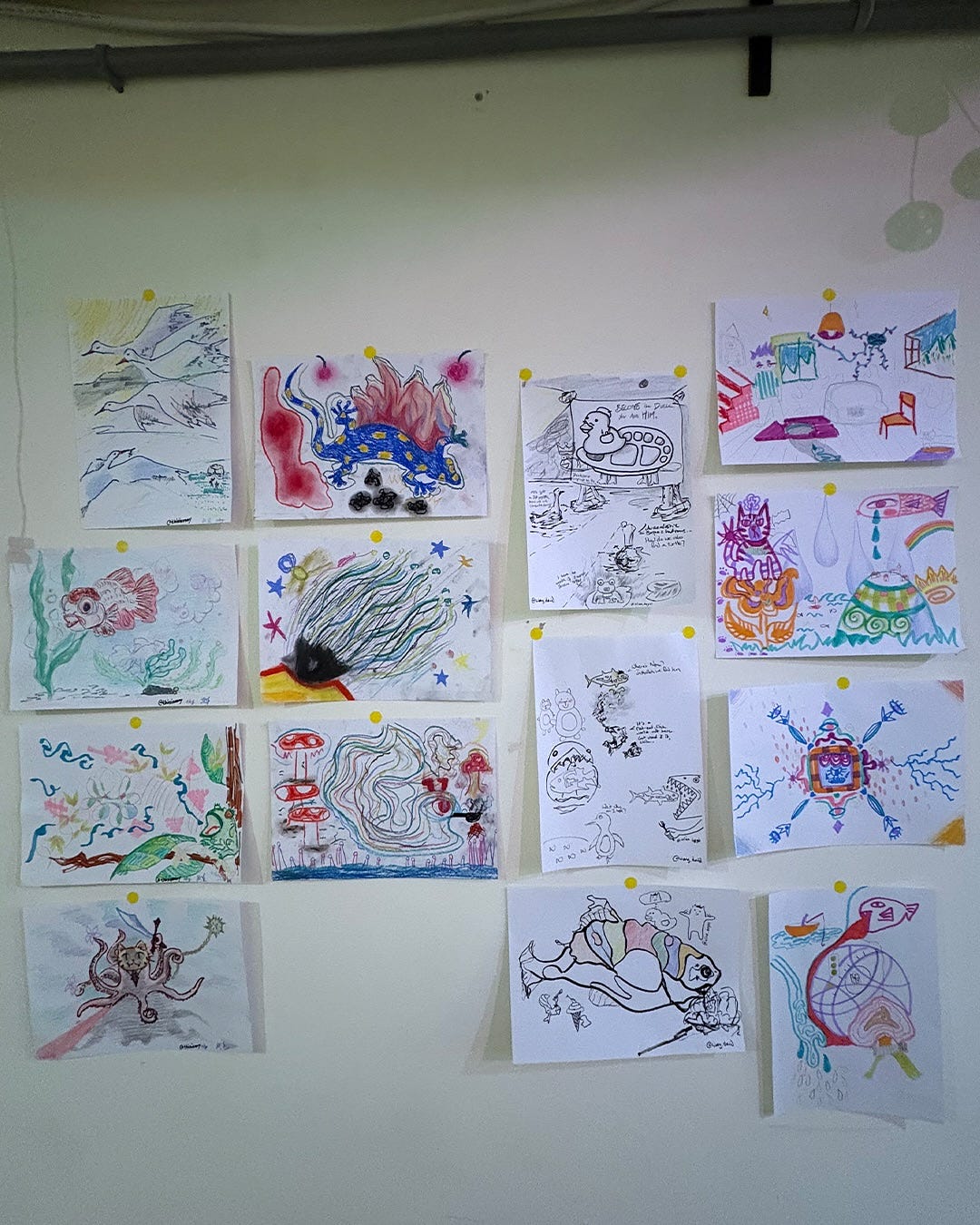 Vertical photo of a room wall full of paper drawings with absurd themes and mixed and matched styles.