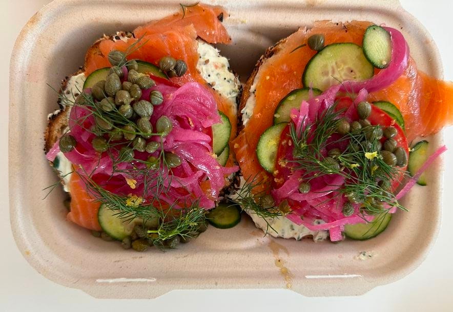 This may contain: two pieces of bread with salmon, cucumbers and onions on them in a plastic container