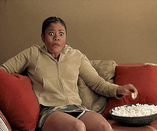 This may contain: a woman sitting on a couch with a bowl of popcorn in front of her face