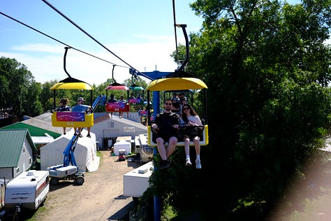 Overhead shot of attendees, friends in the gondola behind me on the Skyride, seed art wall at the Crop Art show, attendee looking over loaves of bread, amusement rides, golden hour behind the crowd, Sweet Martha's Cookies at night.