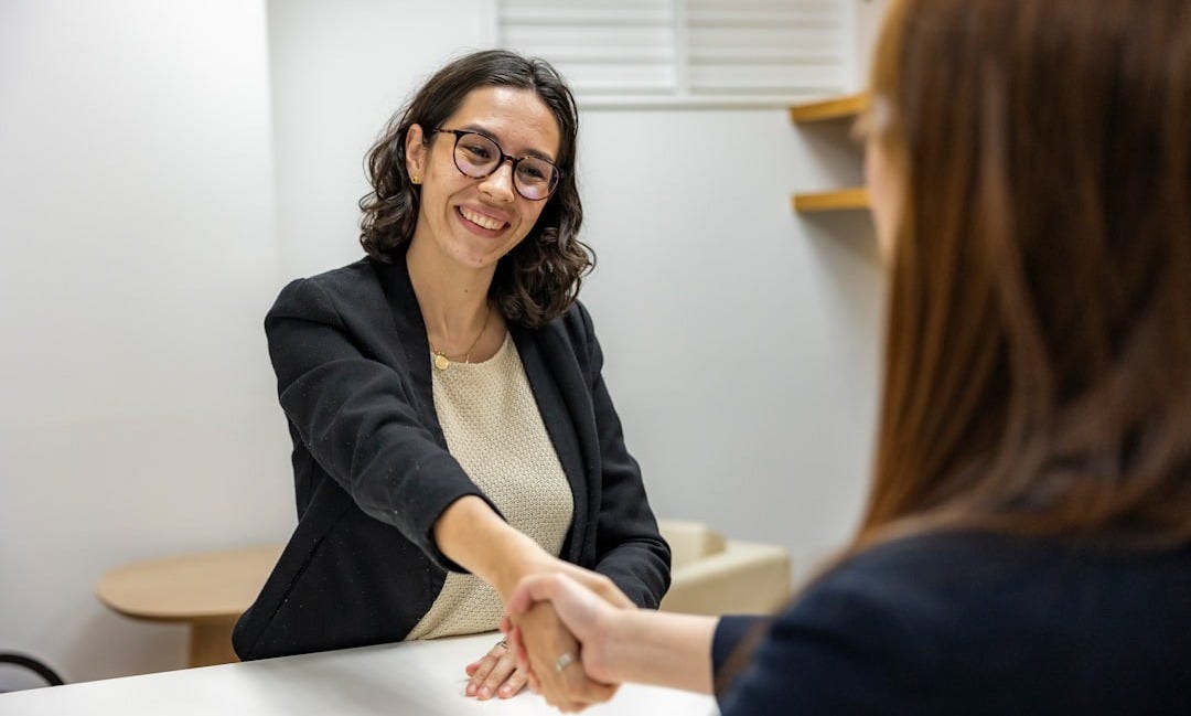 a woman shaking hands with another woman sitting at a table