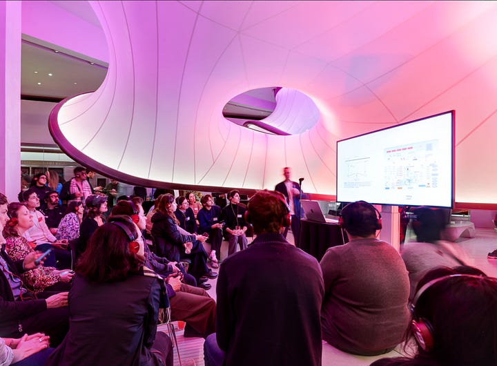 A women in a white blazer delivering a talk to a busy room (left hand side), A man presenting in a pink toned room (right hand side)