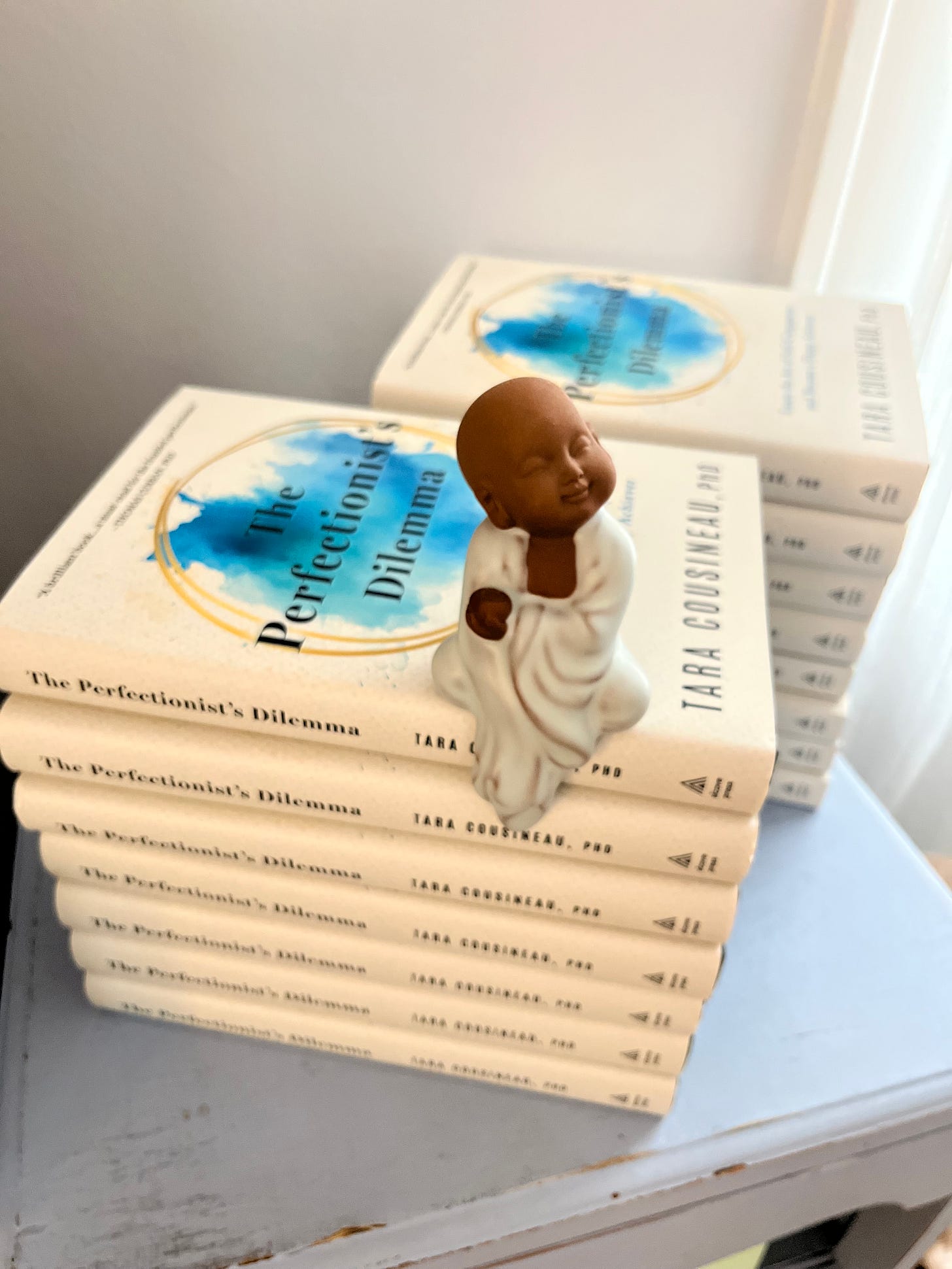 A small Buddha statue on top of a pile of books of The Perfectionist's Dilemma 