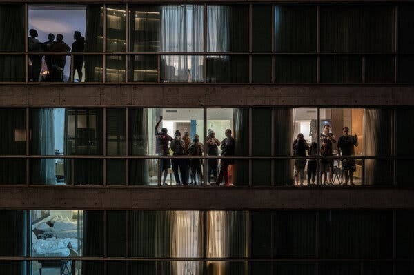 Personas de diferentes pisos de un edificio mirando por las ventanas.