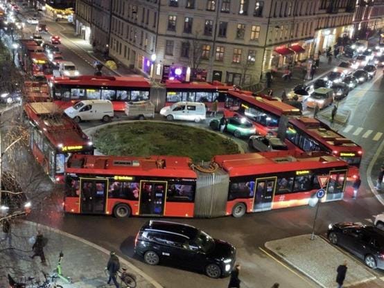 A scene showing four red bendy buses making up a squarw around a small roundabout. There are cars trapped inside them and long lines on the two visible sides going into the roundabout. Photo was found in Avisa Oslo, a local newspaper, and was sent them by a guy named Endre Helgeland. A scene showing four red bendy buses making up a squarw around a small roundabout. There are cars trapped inside them and long lines on the two visible sides going into the roundabout. Photo was found in Avisa Oslo, a local newspaper, and was sent them by a guy named Endre Helgeland.