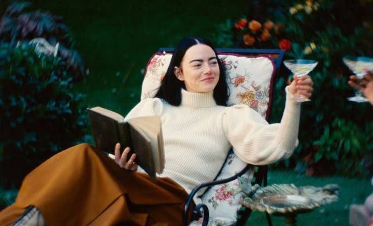 This may contain: a woman sitting in a chair with a book and wine glass next to her head