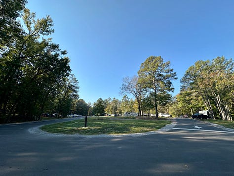 a road with trees, sign for tent sites B18, B19, B20, 3 motorcycles parked in the gravel near the tent sign