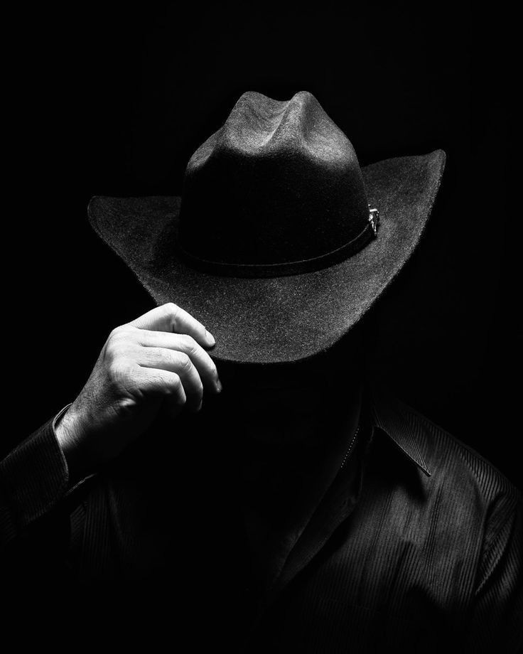 This may contain: black and white photograph of a man wearing a hat with his hand on his face