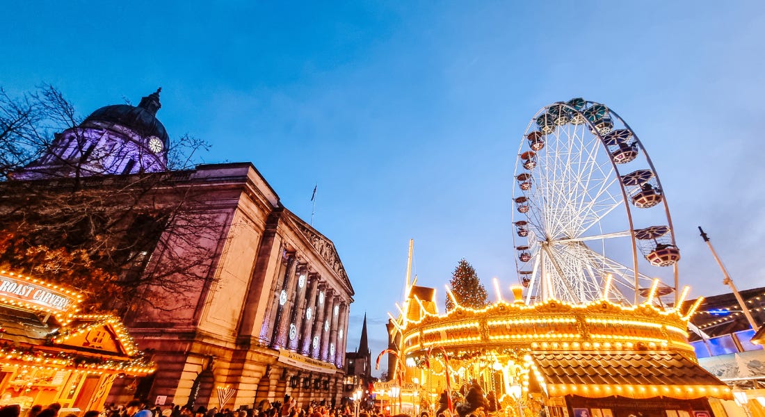 Nottingham's Old Market Square at night with a large grey council house building, lit up stalls, and a lit up merry-go-round