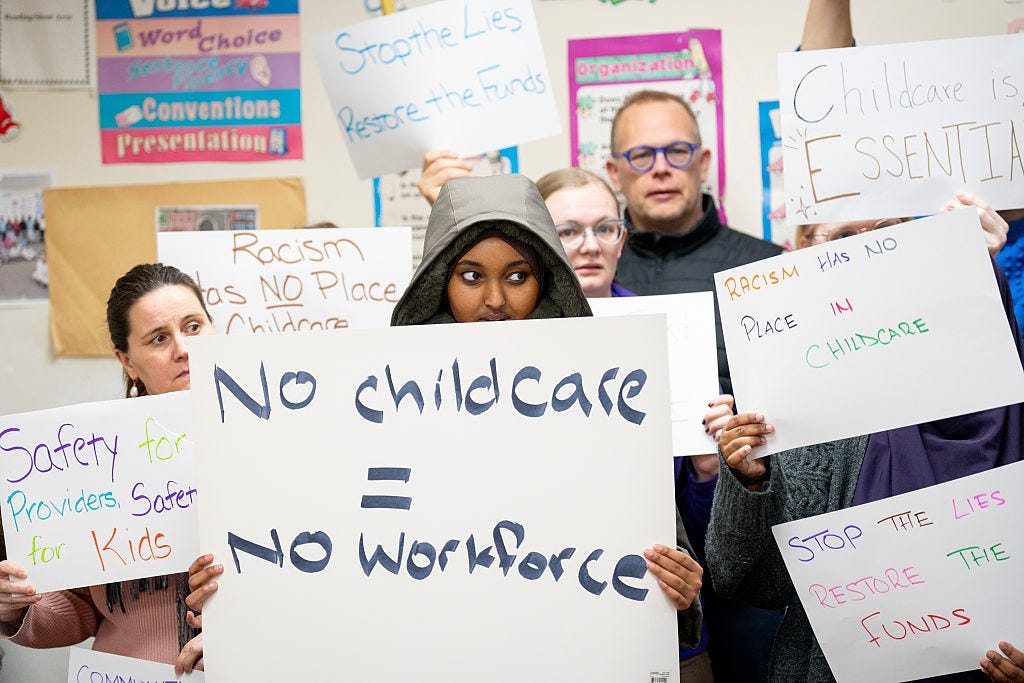 a close up of people holding signs, one brown skinned person in the front wearing a black hood holds a sign that reads “no children = no workforce"