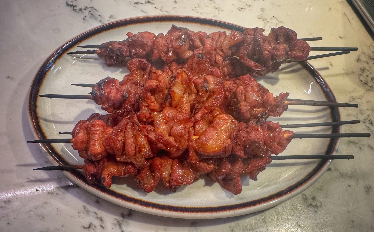 BBQ pork skewers on a serving dish. The pork is somewhat dark and definitely cooked, but it is a far cry from the glossy, dark skewers seen at the Night Market. 