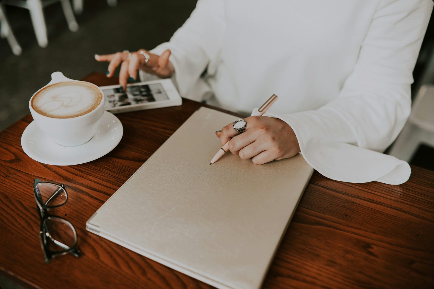 Woman at a desk with a latte, phone, notebook, and pen. Ready for work.