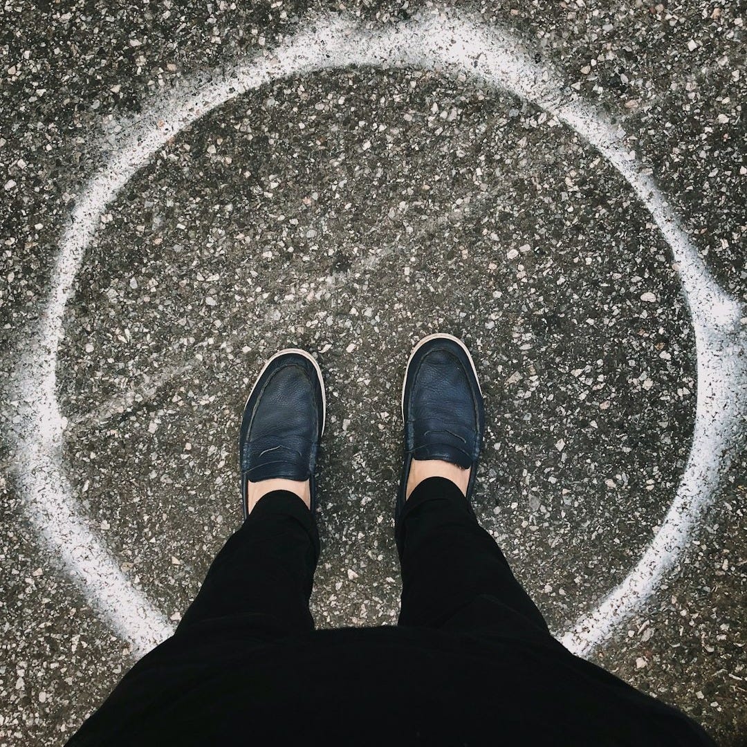 person in black pants and shoes stands inside a white circle