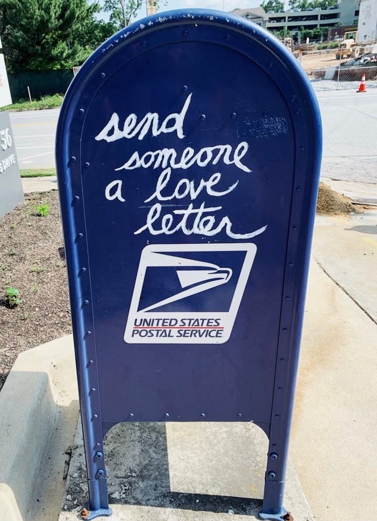 This may contain: a blue mailbox sitting on the side of a road next to a post office
