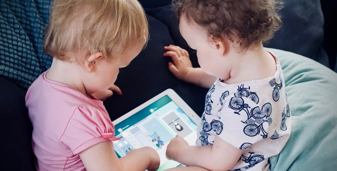 two toddlers sitting on sofa while using tablet computer two toddlers sitting on sofa while using tablet computer