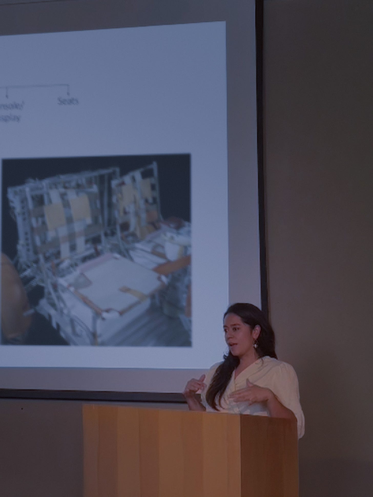 Jess Russi presenting behind a podium and with a projection in the wall in the background