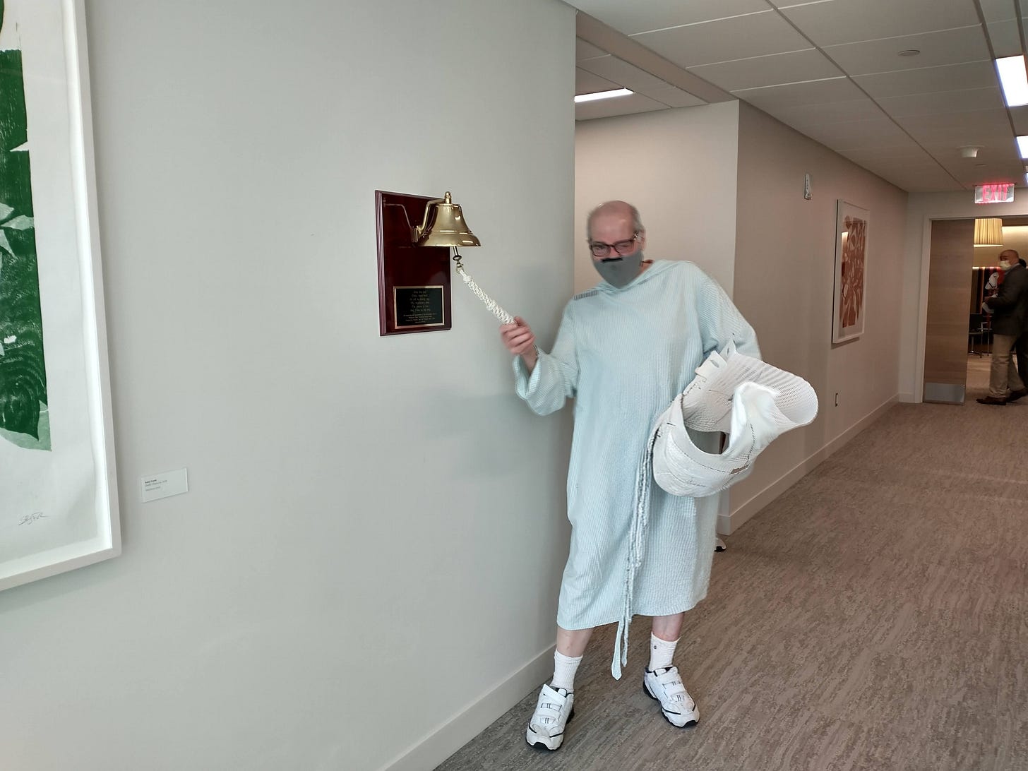 Patient in hospital gown pulls the cord of a brass bell.
