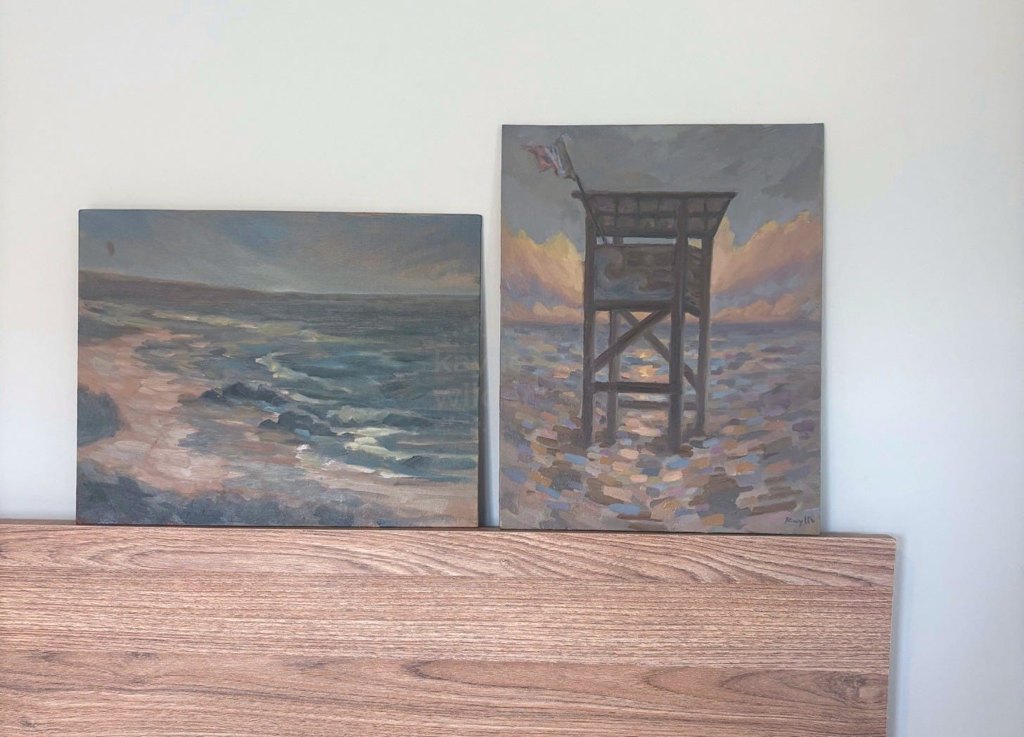 two oceanscape paintings resting on a flat wood bed frame