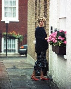 This may contain: a woman standing next to a brick building with flowers in the window boxes on either side