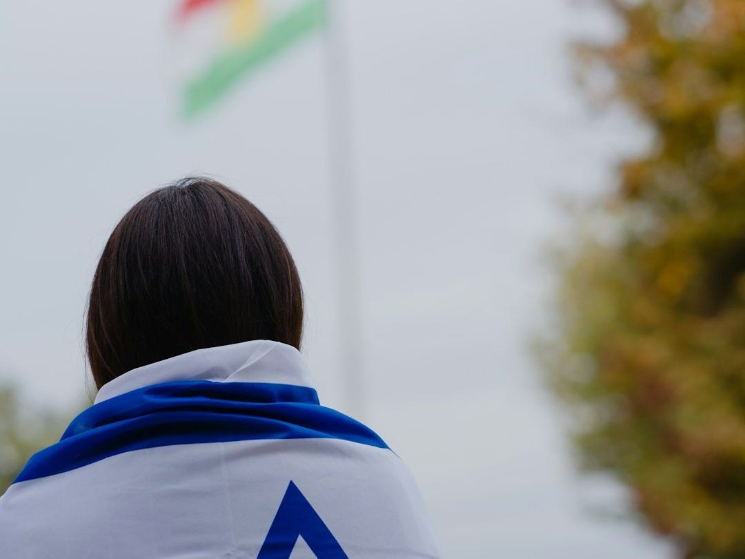 woman in white and blue hoodie standing near green trees during daytime
